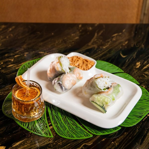 Shrimp and rice spring rolls with peanut sauce and a cocktail garnished with dried orange.