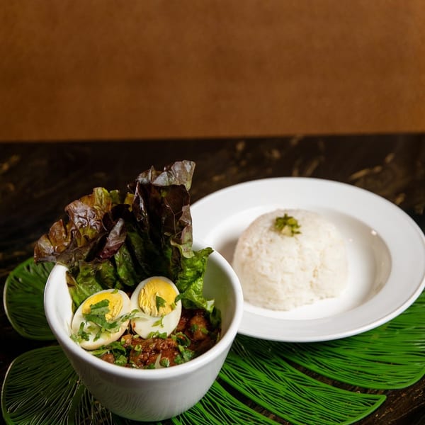 A bowl of stew with lettuce and hard-boiled eggs, served with a side of white rice.